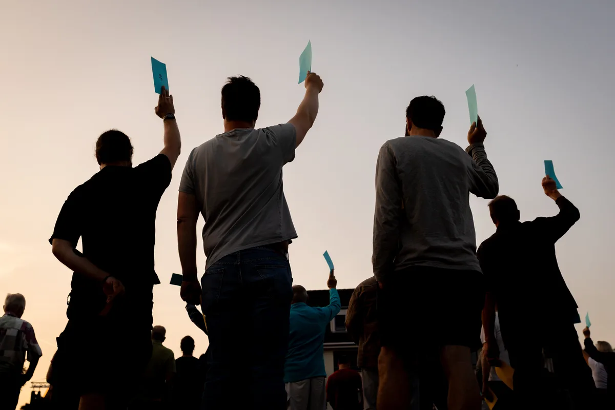 Vier Männer halten ihren blauen Zettel in die Höhe.